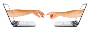 Two human hands coming out two seperate computers, reaching out for each other. Isolated on a white background